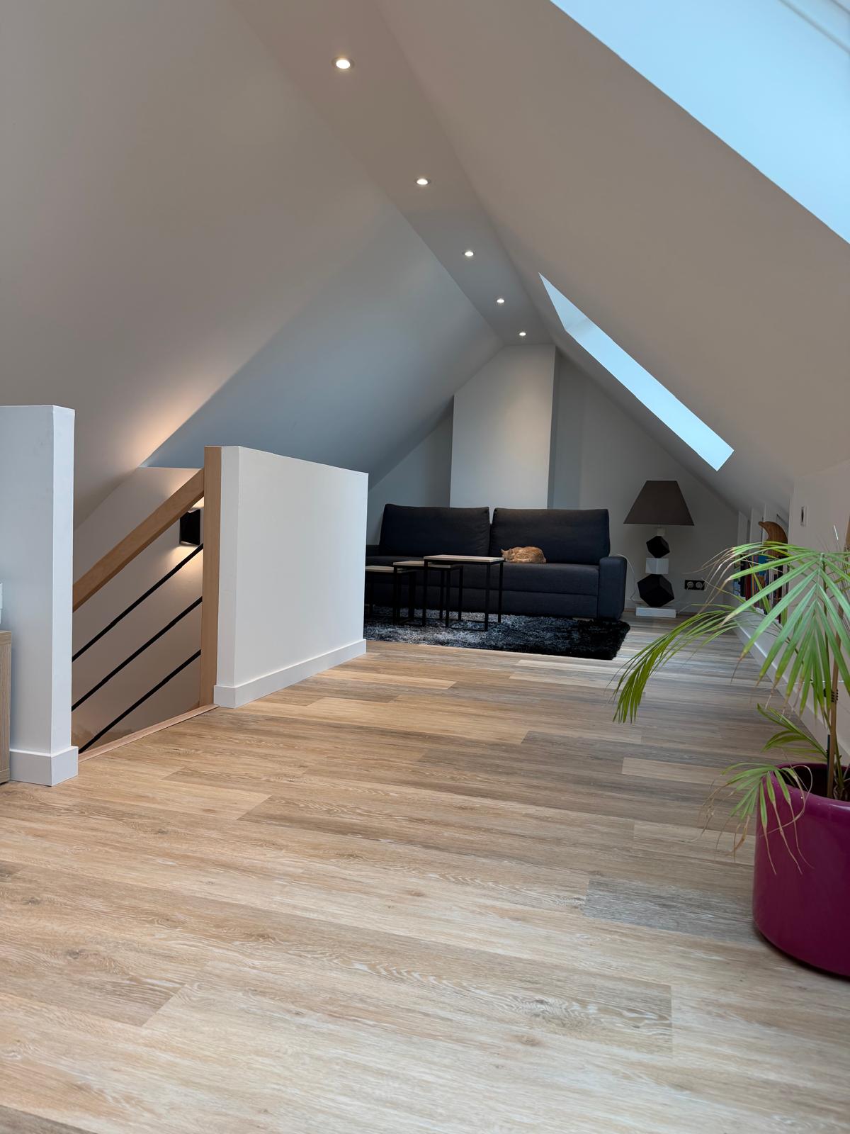 Salon aménagé sous les combles : canapé, escalier et fenêtres de toit